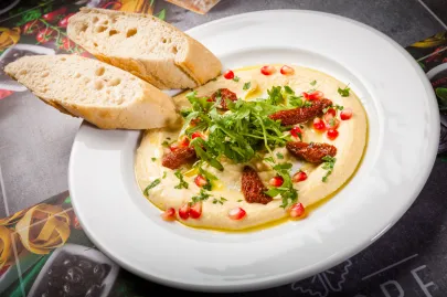 Hummus podawany z granatem, rukolą, suszonymi pomidorami, pietruszką,oliwą i pieczywem