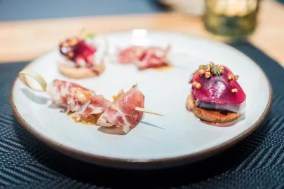 Amuse bouche - karkówka z gorczycą i karmelem oraz śledź ze słoniną i żurawiną, podany na sucharku.