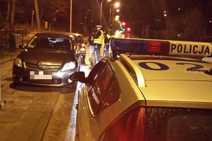 Policja bada alkomatem DJ-a. Jego samochód stoi z tyłu, za autem kierowcy, który go zatrzymał.
