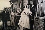 Krystyna i Eugeniusz wraz z weselnikami stoją przy domu rodziny panny młodej.