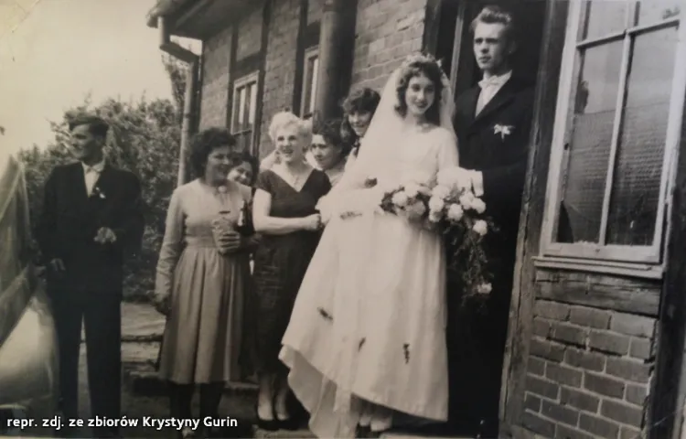 Krystyna i Eugeniusz wraz z weselnikami stoją przy domu rodziny panny młodej.