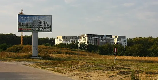 Na pierwszym planie reklama Hossy z nieaktualną już wizualizacją projektu, w oddali powstające osiedle Ekolanu - Apartamenty na Polanie.