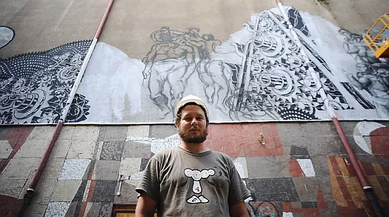 Mariusz Waras na tle muralu na ścianie Kina Neptun, który przygotowuje.