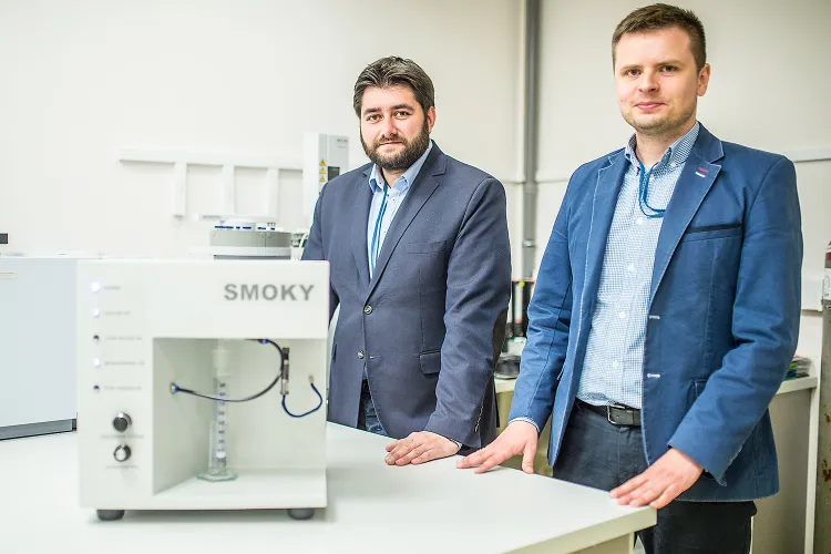 Dr Łukasz Guzik, kierownik Działu Analiz Farmaceutycznych Spark - Lab i Maciej Barc, wiceprezes zarządu z maszyną Smoky - Lab, umożliwiającą badanie aerozolu wygenerowanego z e-liquidu w warunkach zbliżonych do rzeczywistego używania e-papierosa. 