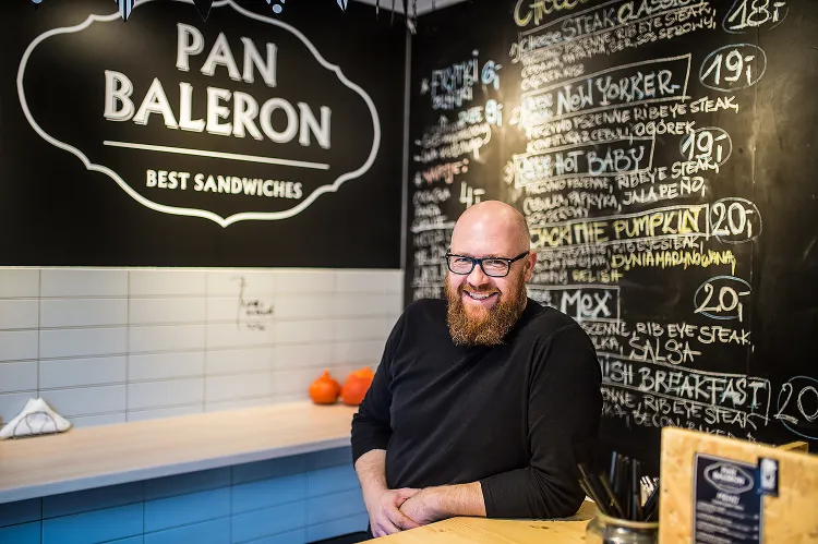 Pan Baleron podaje Philly Cheese Steak Sandwich, czyli kanapki z siekaną wołowiną, serowym sosem i przeróżnymi dodatkami.