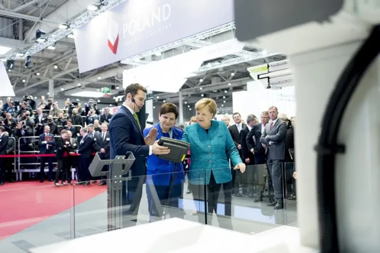 Premier Beata Szydło i kanclerz Angela Merkel grają w kółko i krzyżyk z robotem kartezjańskim TMA Automation. Robota prezentuje Piotr Orlikowski, wiceprezes gdyńskiej firmy. 