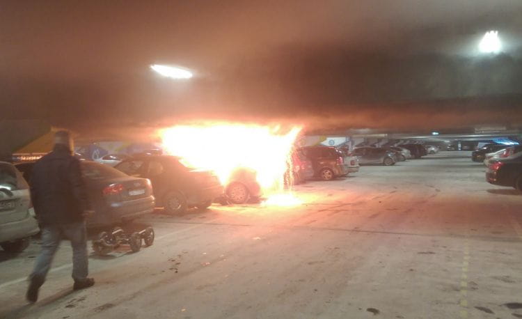 Płonące pojazdy na parkingu w centrum handlowym.