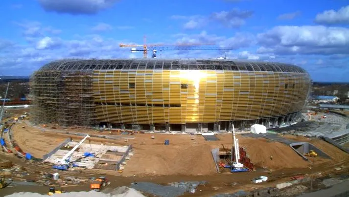 PGE Arena Gdańsk błyszczy w słońcu niczym grudka bursztynu wyrzucona na morski brzeg. Zdjęcie z kamery internetowej na placu budowy stadionu w Letnicy.