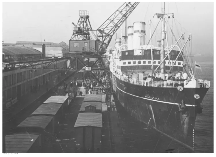 Statek pasażerski s/s "Kościuszko" widoczny od strony dziobu podczas przeładunku w porcie w Gdyni. Widoczne portowe urządzenia przeładunkowe oraz wagony kolejowe.