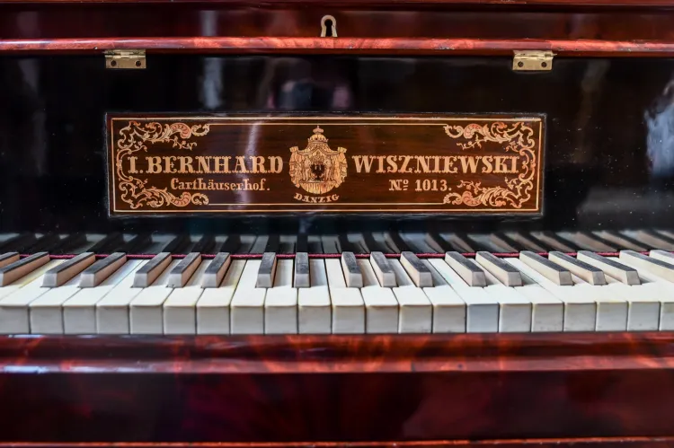 Zdjęcie przedstawia klawiaturę najstarszego gdańskiego fortepianu z około 1830 roku. Nad klawiaturą znajduje się tabliczka znamionowa firmy Wiszniewskich w języku niemieckim: I. Bernhardt Wiszniewski, Carthauserhof, no 1013.