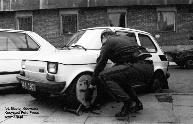 Strażnik miejski zakłada blokadę na koło nieprawidłowo zaparkowanego malucha, czyli fiata 126p. Zdjęcie wykonano przy ul. św. Ducha w Gdańsku w październiku 1992 r.
