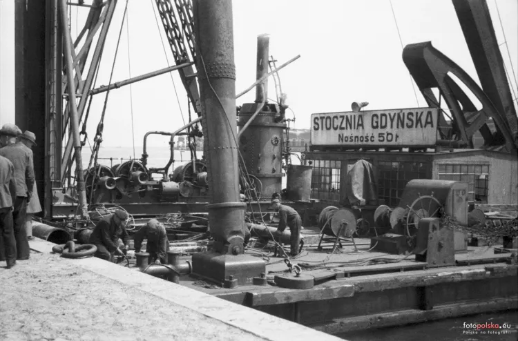 Zdjęcie wykonane na terenie Stoczni Gdyńskiej w 1936 r., kiedy to nad wieloma jej pracownikami wisiała opisana w artykule groźba zwolnienia. Pośrodku widoczny dźwig pływający.