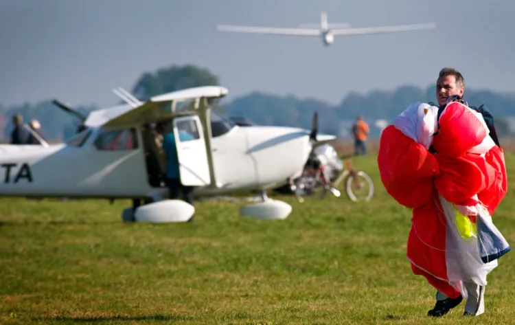 Typowy dzień z życia aeroklubu. Skoczek niesie swój spadochron, w tle samolot przygotowujący się do startu i szybowiec podchodzący do lądowania.