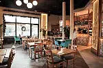 Wnętrze restauracji jest jasne i przestronne, utrzymane w piaskowych kolorach oraz odcieniach szarości i zieleni z elementami drewna.