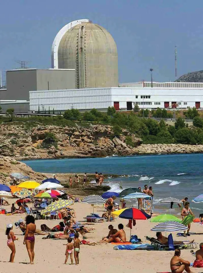 La foto muestra una playa en Vandelos, España.  Central nuclear en la distancia. 