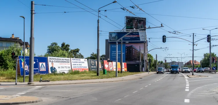 Skrzyżowanie ulicy Wielkopolskiej i alei Zwycięstwa: przyczepy, bilbordy, stelaże i reklamy na ścianie budynku.