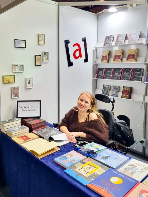 Sylwia Błach podpisuje książki podczas jednych z targów książki. 